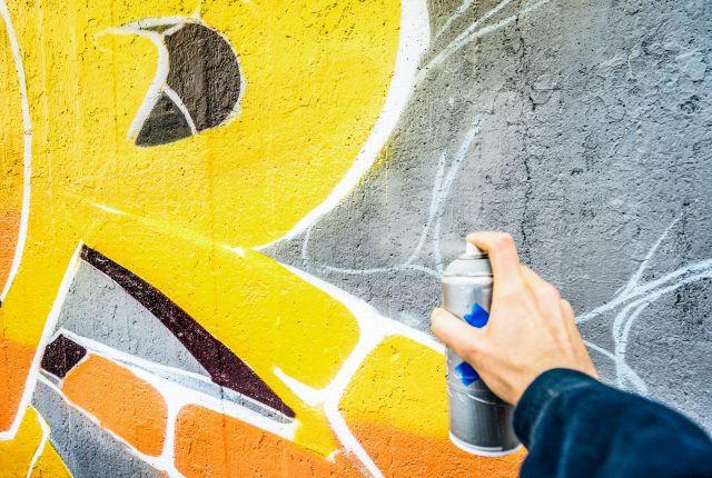 Detail of street artist painting colorful graffiti on public wall - Modern art concept with urban guy drawing live murales with multi color aerosol spray - Vintage filter with focus on yellow paint